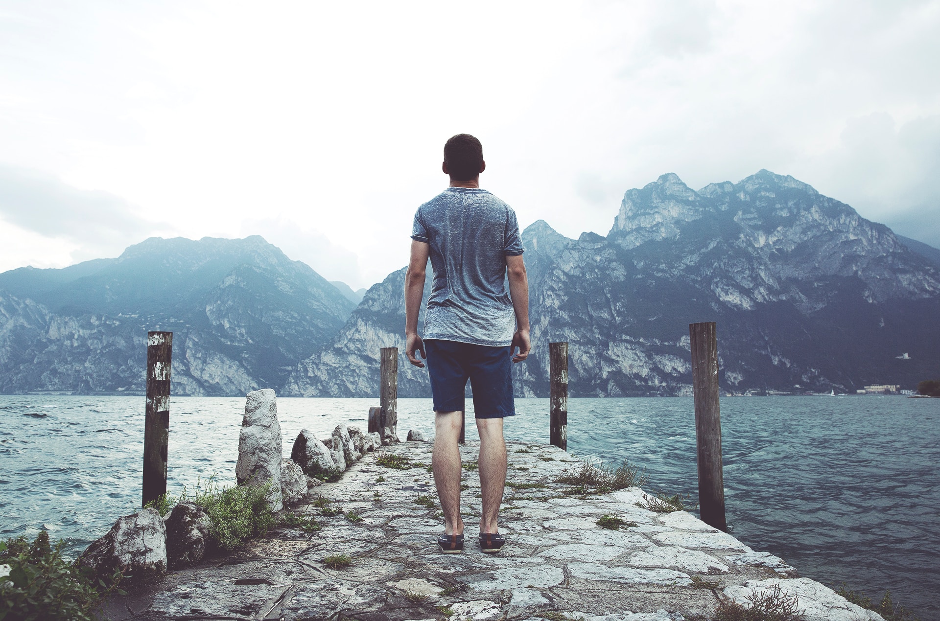 Young man standing alone on a pier facing a mountain