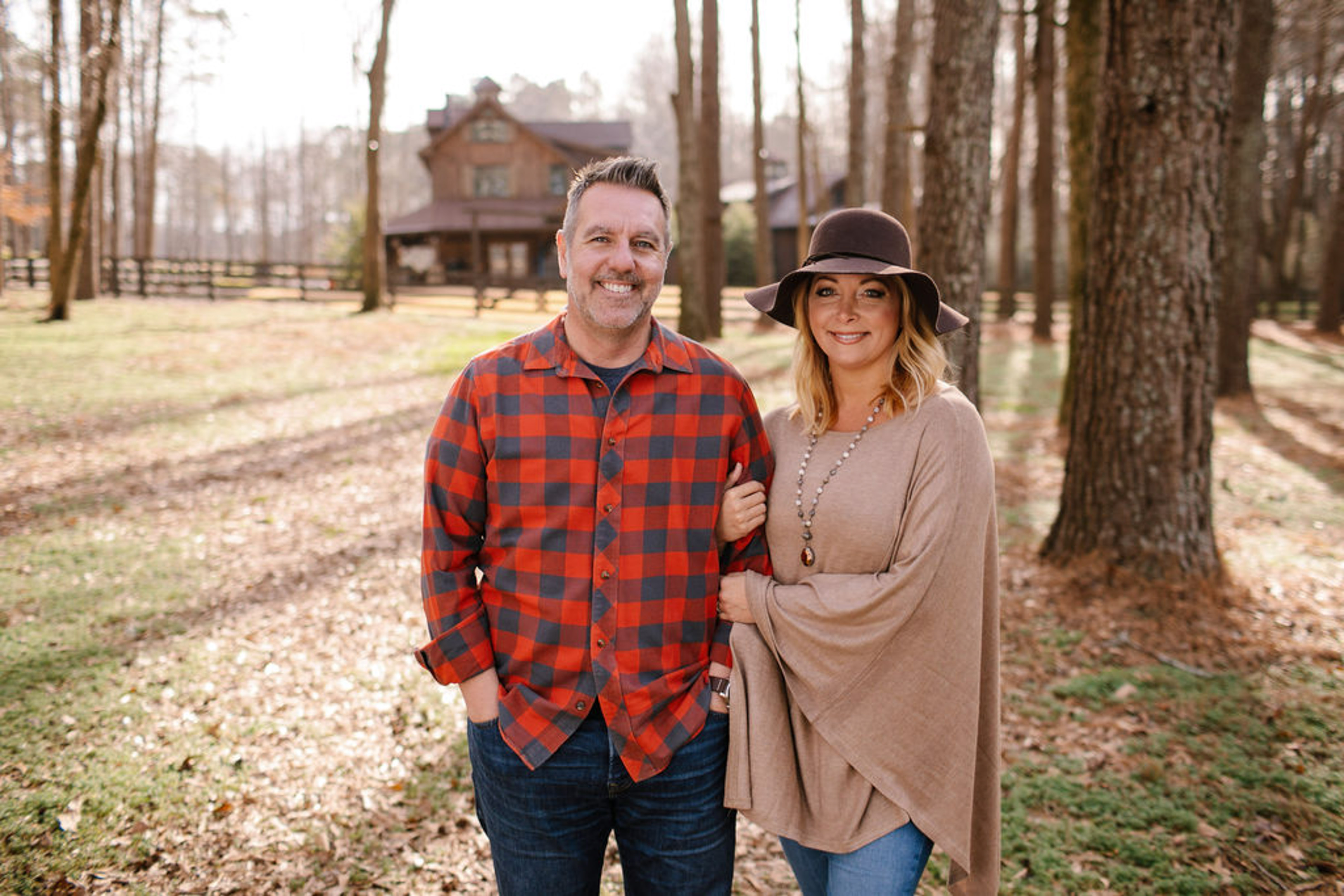 Shannon & Bryan Miles married entrepreneurs, standing together linked arms in wooded area in front of home