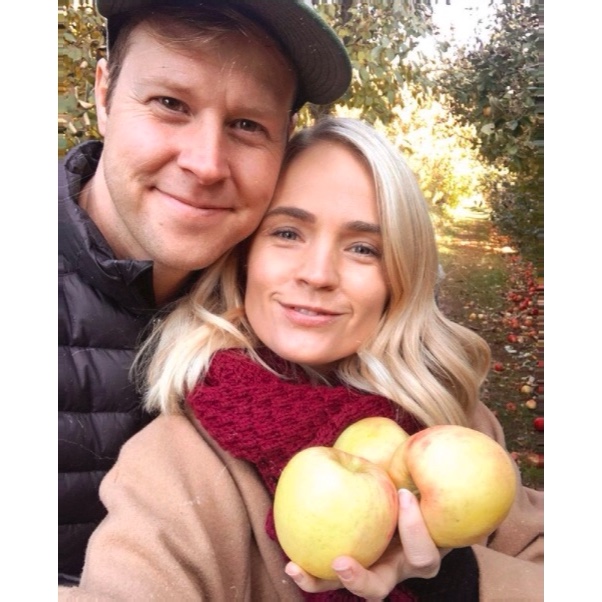 young couple in fall attire, holding apples they picked